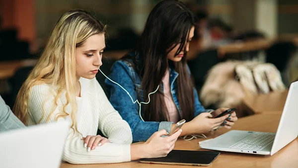 Eine Person schaut auf ihr Smartphone, eine andere auf ihren Laptop
