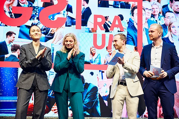 Vier Studierende stehen auf einer Bühne und klatschen.