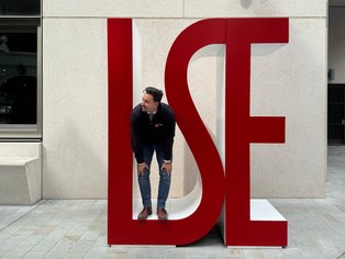 UW/H-Alumnus Marlon Warrach ist für seinen Master an die London School of Economics and Political Science (LSE) gegangen. (Foto: privat) Marlon steht in großen roten LSE-Buchstaben.