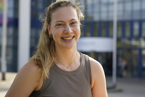 Porträt einer jungen Frau vor einem Universitätsgebäude.