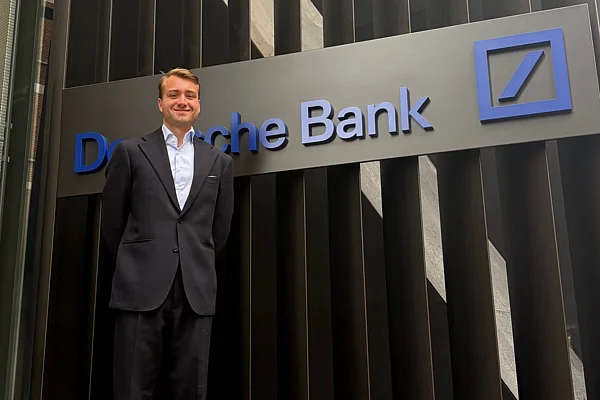 Ein Mann im Anzug steht vor dem Gebäudeschriftzug der Deutschen Bank.