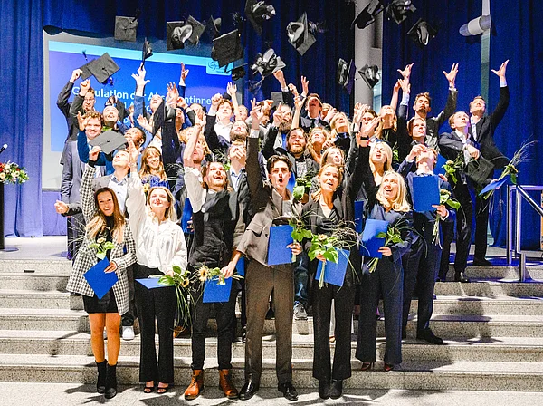 Gruppenfoto von Absolvent:innen, die ihre Hüte in die Luft werfen.
