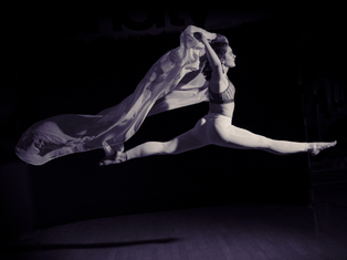 Schwarzweiß-Aufnahme einer Tänzerin, die in der Luft einen Spagat macht.