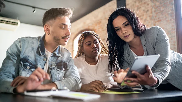 Eine Frau zeigt zwei jüngeren Personen etwas auf einem Tablet
