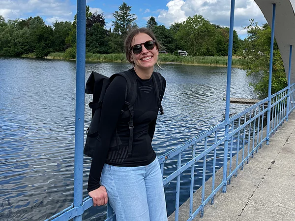 Carlotta Fehrmann lehnt an einer Brücke und lächelt in die Kamera.