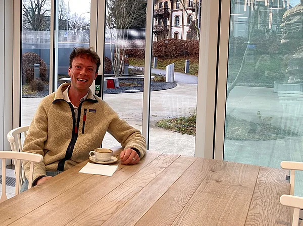 Victor Wolff sitzt mit einer Tasse Kaffee an einem Holztisch.