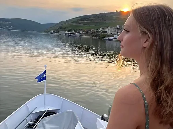 Pia Klee steht am Bug eines Schiffes und schaut über einen Fluss in den Sonnenuntergang.