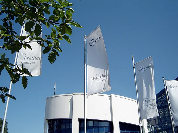 Freiheit, Wahrheit, soziale Verantwortung: Die Grundwerte der UW/H wehen auf Fahnen vor dem Campusgebäude.