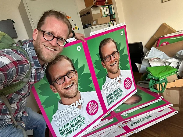 Ein Mann posiert für ein Foto zusammen mit zwei Wahlplakaten von ihm.