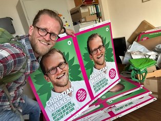 Bei der Kommunalwahl im September 2025 tritt Christian für das Bündnis 90/Die Grünen an. (Foto: privat) Ein Mann posiert für ein Foto zusammen mit zwei Wahlplakaten von ihm.