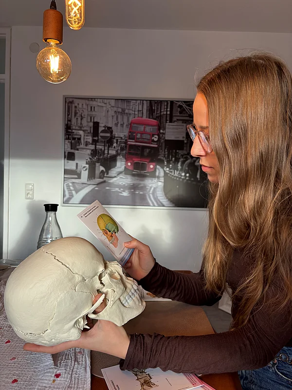 Alicia hält einen Schädel in der Hand und gleicht ihn mit einer Abbildung ab.